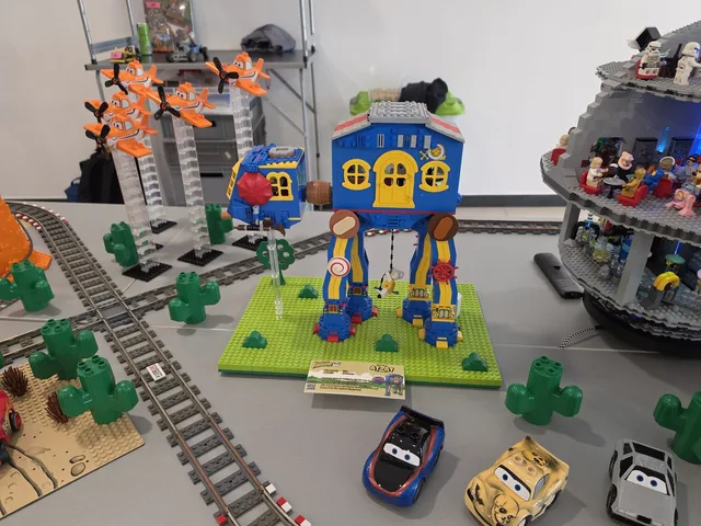 Ein AT-AT im Fabuland-Stil: blauer Körper, gelbe runde Fenster, auf einer grünen Bauplatte neben Duplo-Fahrzeugen und einem grauen Todesstern