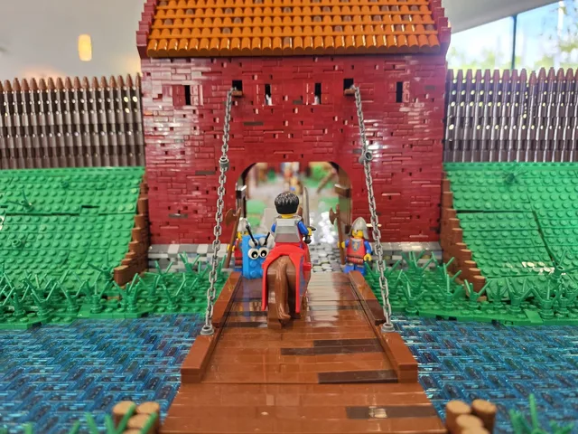 Nahaufnahme eines roten Burgtors aus LEGO mit hölzerner Zugbrücke über einem Wassergraben