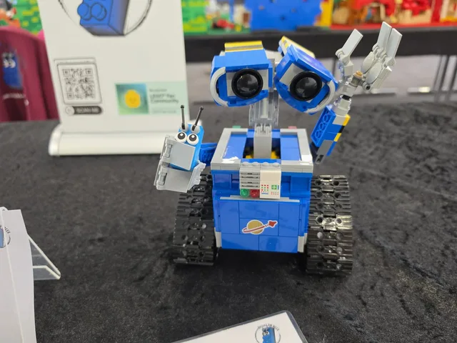 Ein blauer Roboter aus LEGO-Steinen mit großen Augen, daneben das Maskottchen von Bricks am Meer